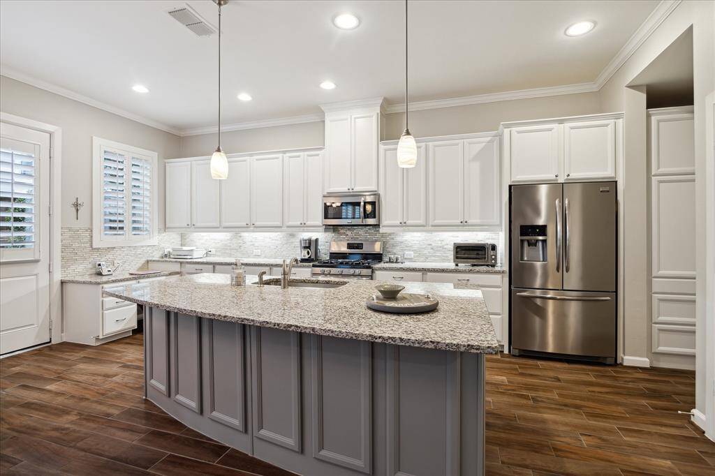 This kitchen features a spacious layout with amazing storage space, large granite island is perfect for prep space. The room is well-lit with recessed lighting and pendant lights, complemented by a stylish tile backsplash. Rivals' new construction with current color palate and trends.