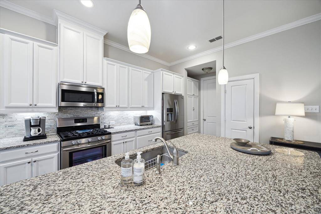 This modern kitchen features white cabinetry.  Walk in pantry as well as an additional pantry added with pull out drawer for additional storage and function. It's well-lit with pendant lighting and has a sleek, clean design perfect for entertaining and cooking. The left door is to the attached garage.