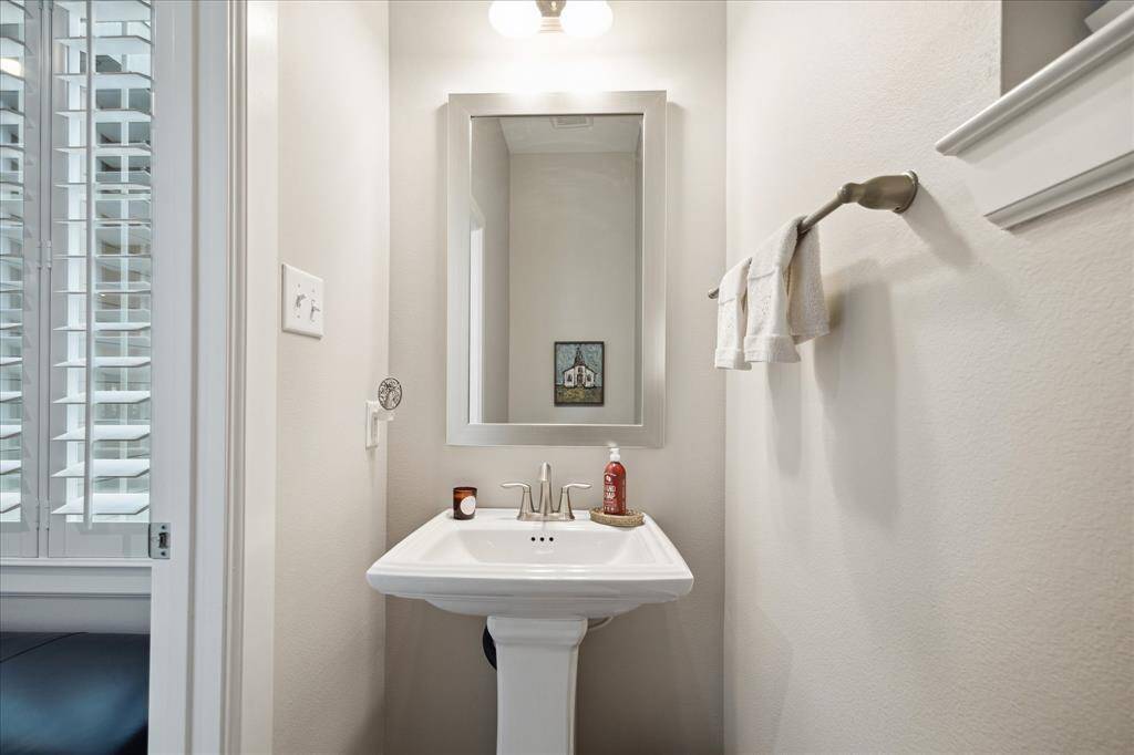 Powder room tucked away from the entry is well-lit with a pedestal sink, a framed mirror, and a towel rack. It features neutral-colored walls and modern fixtures.