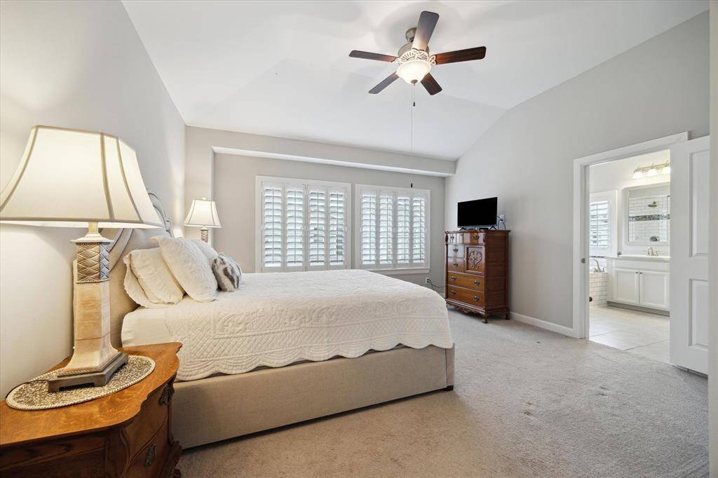 This spacious bedroom features a cozy carpeted floor, a ceiling fan, and ample natural light from large windows with shutters. High ceiling and stylish framed windows. Ideal for comfort and relaxation.