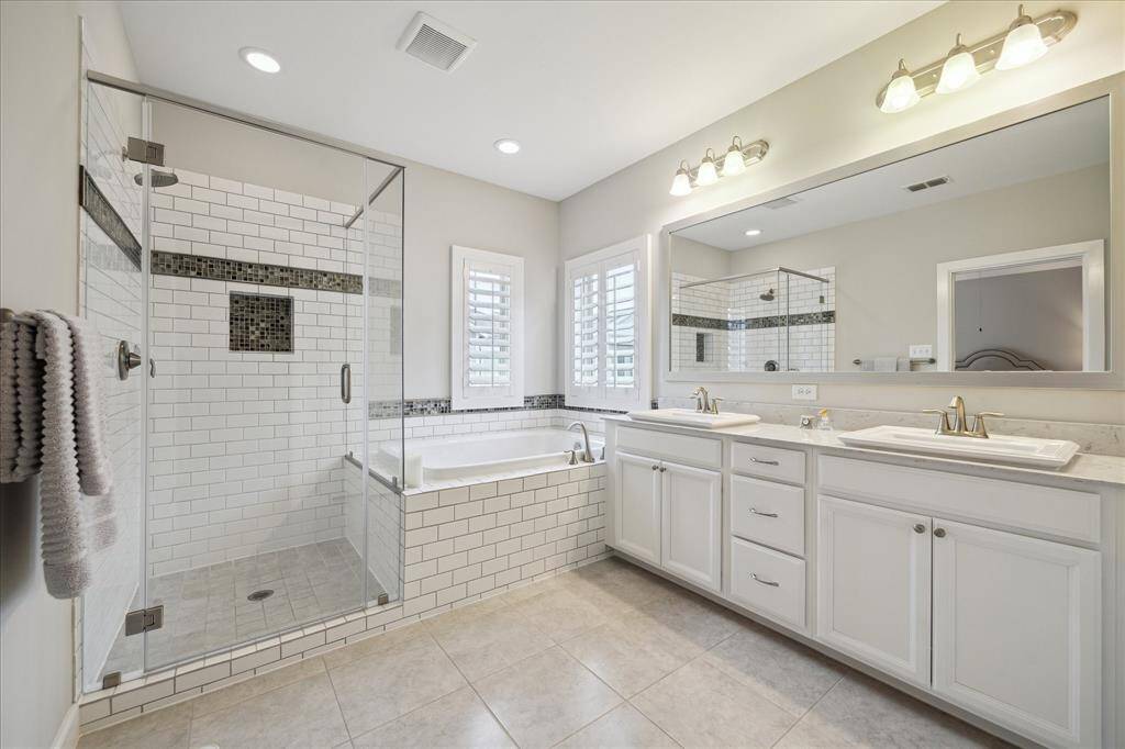 This bathroom features a spacious glass-enclosed shower, a large soaking tub, and dual sinks with ample counter space. The design includes modern fixtures, a neutral color palette, and plenty of natural light.