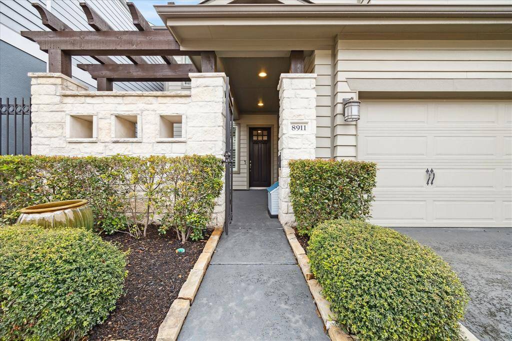 This inviting entrance features a covered porch with stone pillars, neatly trimmed hedges, and a charming walkway leading to the entrance. The garage is adjacent, providing convenient access.