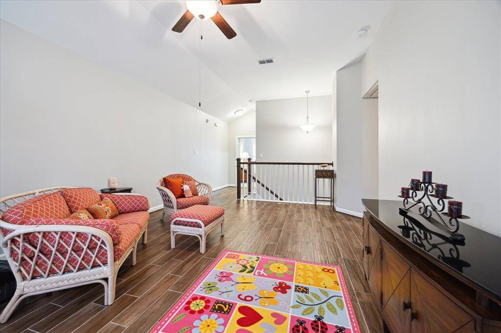 This spacious living area features a vaulted ceiling with a ceiling fan and modern wood-look flooring. The room is well-lit with natural light and has an open view to the hallway and staircase. The home is spacious enough for a family and offers flex space.