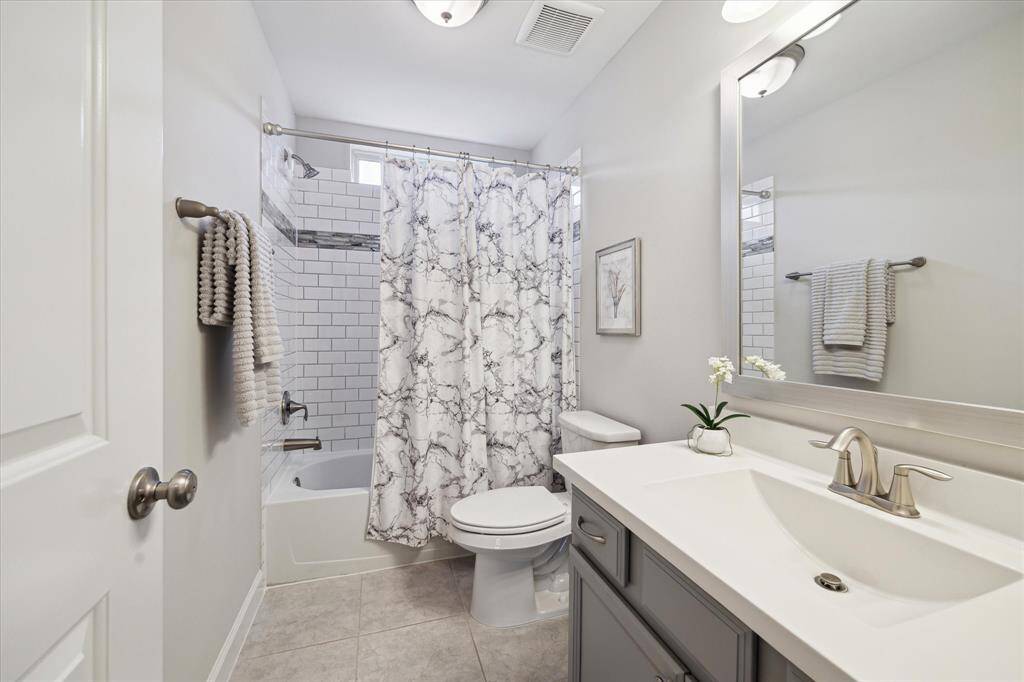 Secondary bathroom with large vanity sink, neutral upgraded tile in the shower area with transom window for added light.