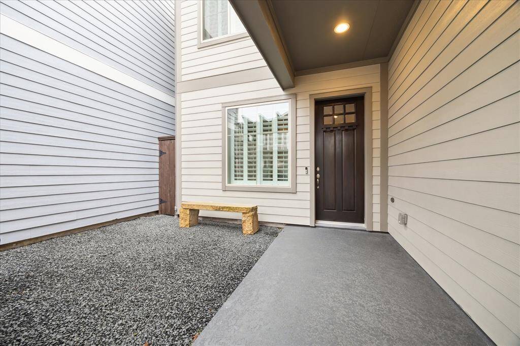 Front patio for outdoor entertaining. This covered entryway with light-colored siding and a dark front door. The area features a gravel section for low maintenance, offering a clean, welcoming atmosphere.