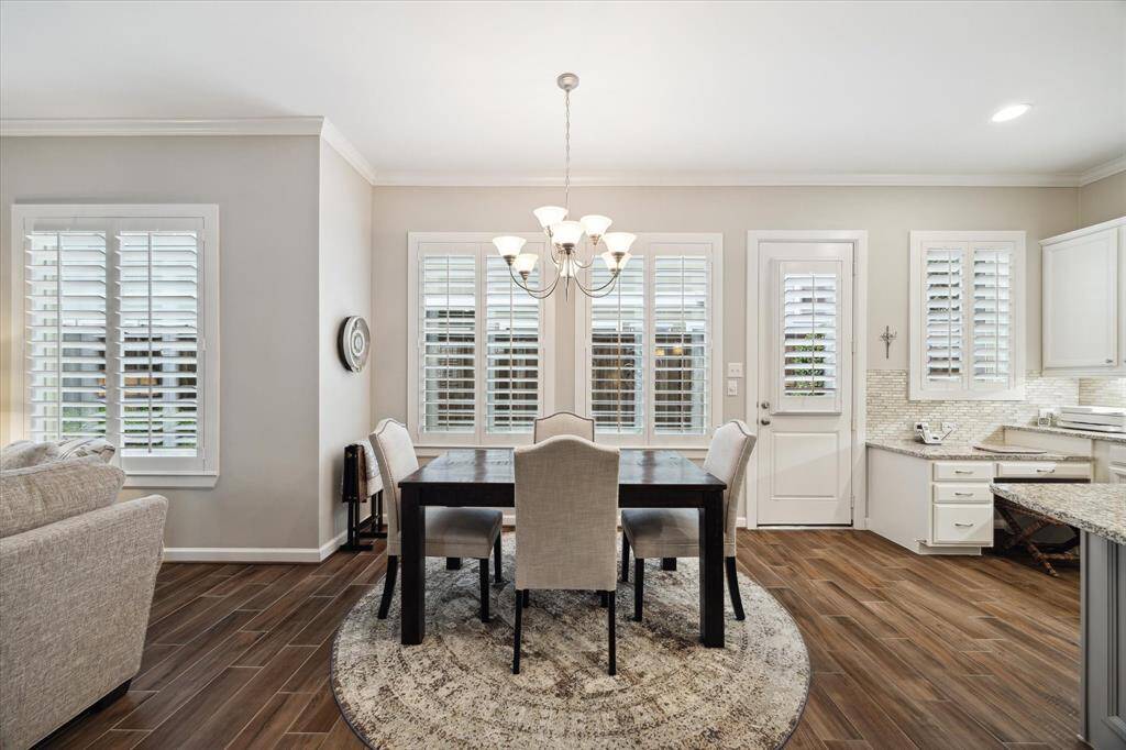 Bright dining area with large windows and shutters and a door to another outdoor space. The open layout flows into a stylish kitchen with sleek white cabinets and granite countertops.