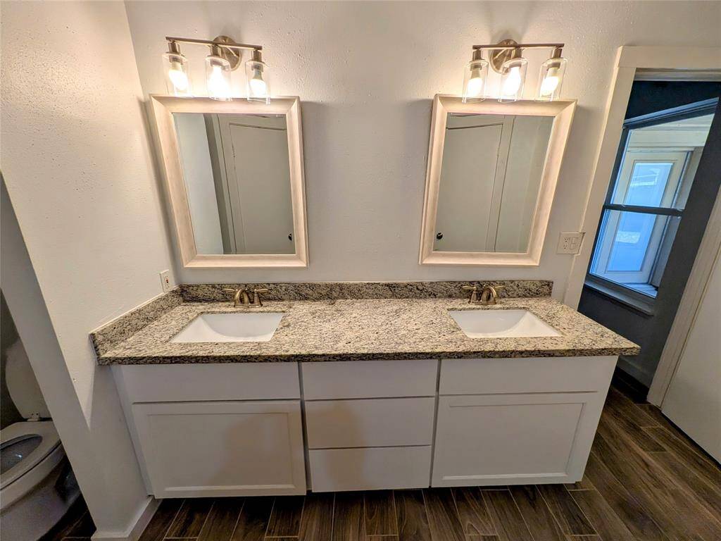 This bathroom features a double vanity with granite countertops, framed mirrors, and modern light fixtures.
