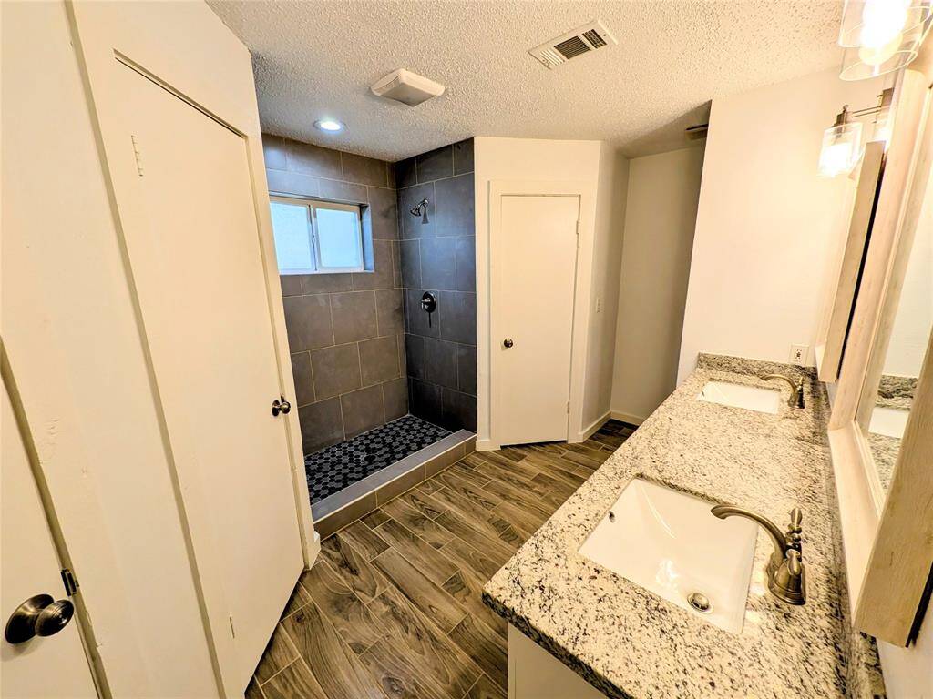 This bathroom features a spacious walk-in shower with modern gray tiles and a pebble floor. It includes his and hers closet with sensor light bulbs