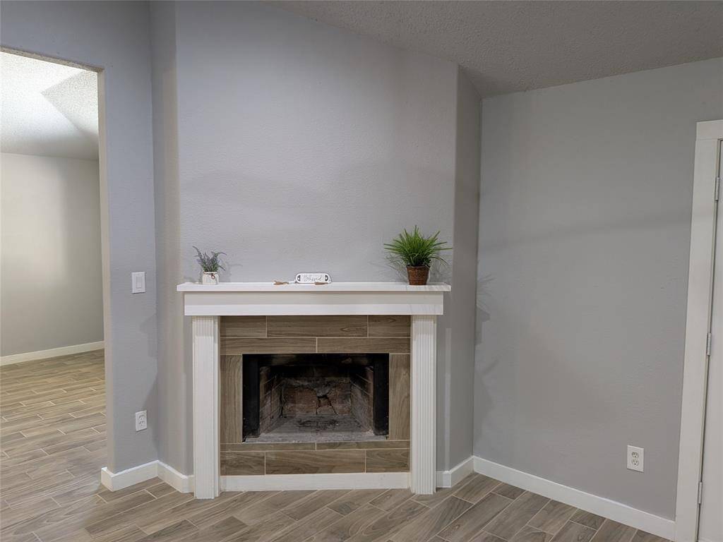 Cozy corner with a fireplace featuring a light mantel and tile surround. The walls are painted in a neutral gray, and the floor has wood-like tiles, creating a warm, inviting atmosphere.