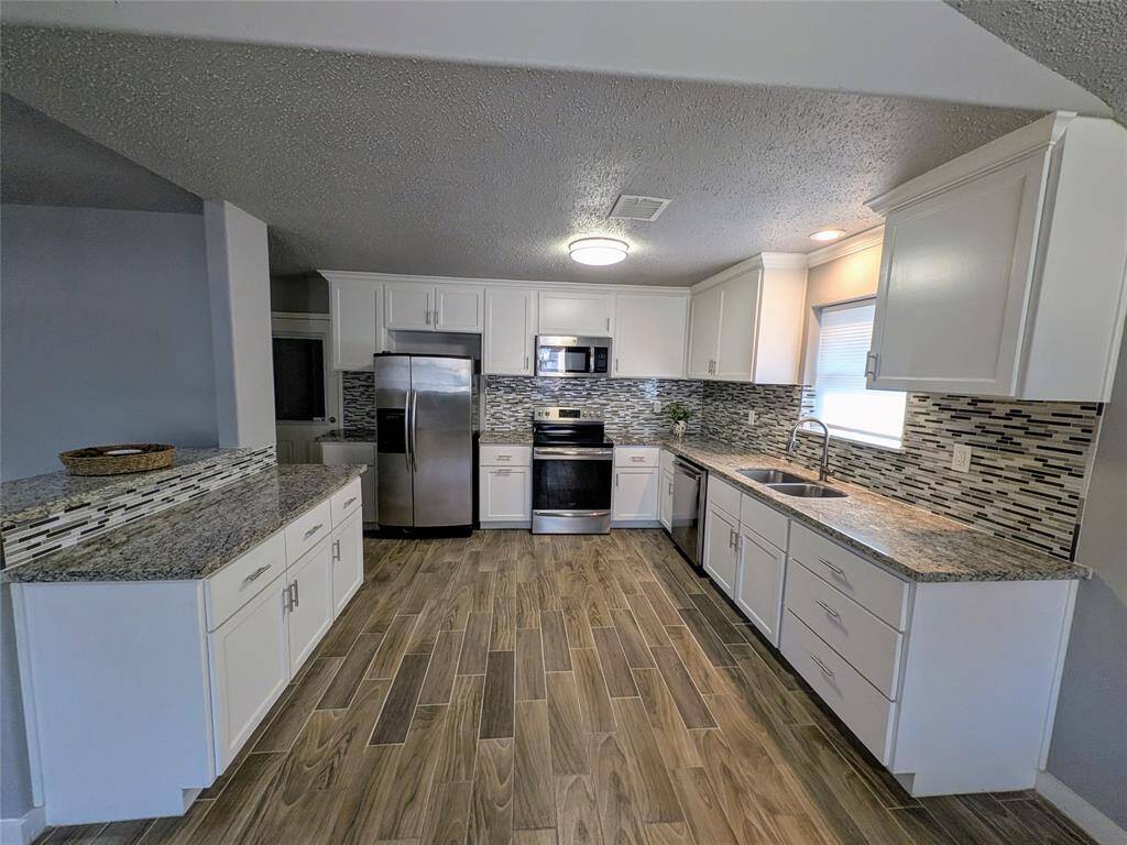 This kitchen features modern white cabinetry, stainless steel appliances, and granite countertops. The backsplash adds a stylish touch, and the wood-look tile flooring enhances the contemporary feel. Ample natural light streams in, creating a bright and inviting space.