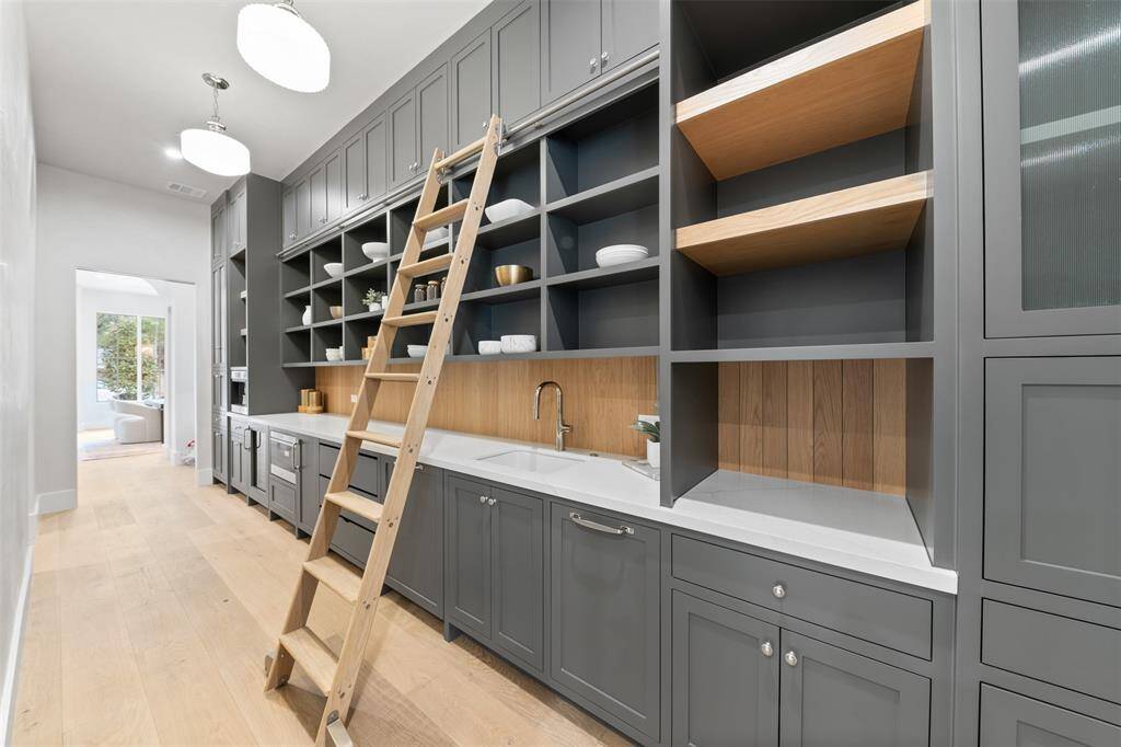 A rolling ladder adds a touch of classic charm while providing easy access to upper shelves. For convenience, a water bottle filler is discreetly installed, ensuring hydration is always within reach. An icemaker stands ready for entertaining, while a dedicated coffee bar area offers a stylish, serene spot for morning brews or after-dinner indulgences. Every detail in this thoughtfully designed space elevates the home’s functionality while maintaining a sophisticated, polished feel.