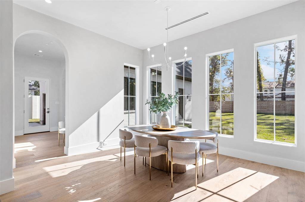 This custom-built luxury breakfast area is a bright, inviting space that seamlessly blends style with comfort. A stunning designer light fixture hangs overhead, casting a warm, elegant glow across the room. Grand windows surround the space, allowing natural light to flood the area while offering breathtaking views of the outdoors.