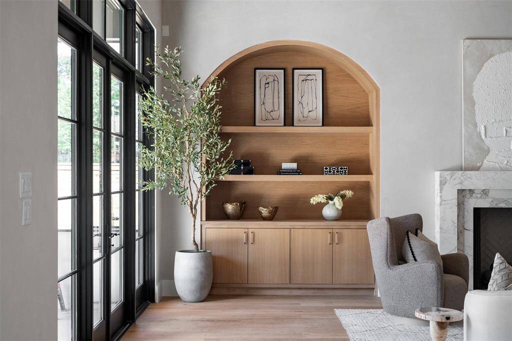 This living room exudes timeless elegance and sophistication. The focal point is the hand-crafted built-ins, meticulously designed with art lighting that showcases curated pieces and adds a gallery-like feel to the space. The room boasts grand height ceilings that amplify its sense of openness and airiness, further enhanced by the seamless flow into the adjacent kitchen.
