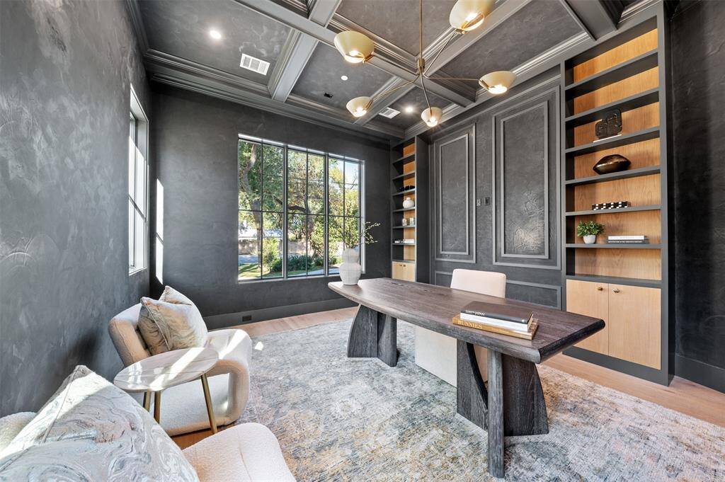 This luxury office space exudes elegance and professionalism. A coffered ceiling adds architectural sophistication, drawing the eye upward and creating a sense of grandeur. The striking black Venetian plaster walls set a bold, dramatic tone, while custom-built shelving and cabinetry provide both style and functionality for storing books, documents, and personal touches.