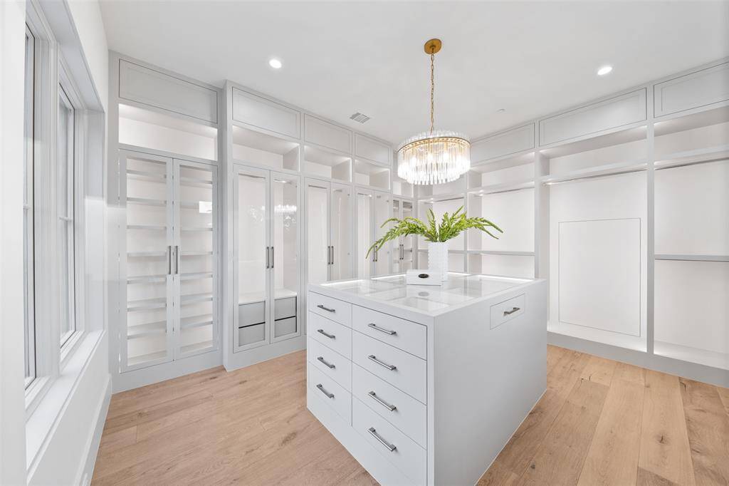 This luxury primary walk-in closet is a true masterpiece of organization and design. Each glass-enclosed cabinet is illuminated with sleek downlighting, highlighting your wardrobe in a soft, elegant glow. The carefully arranged shelves and drawers offer abundant storage for clothing, accessories, and shoes, while the high-end finishes and attention to detail elevate the entire space.