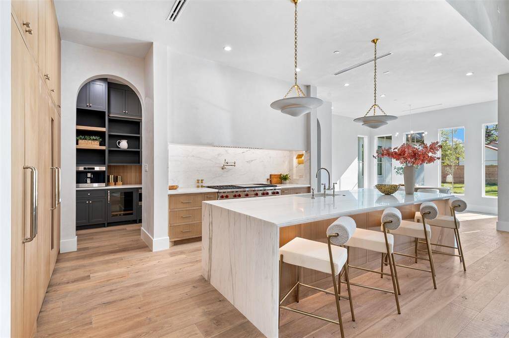 The centerpiece is a double-sized island with a stunning waterfall edge, crafted from premium stone that flows elegantly to the floor.