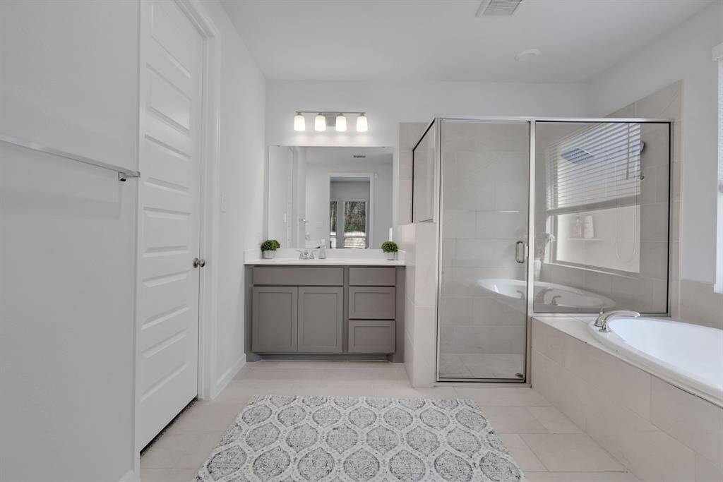 Bright and spacious bathroom featuring a glass-enclosed shower, a large soaking tub, and a wide vanity with ample storage. The neutral tile and sleek fixtures create a relaxing atmosphere.