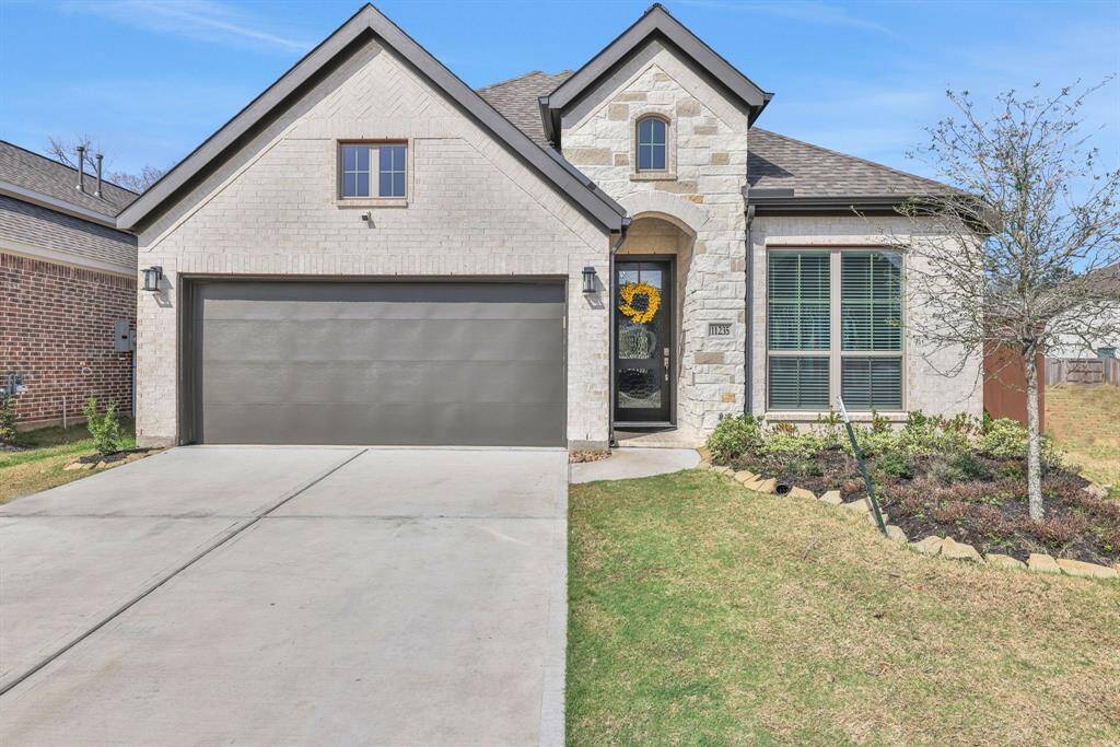 MOVE IN READY!! Charming single-story home with a modern brick and stone exterior, featuring a two-car garage and a welcoming front entrance. The well-maintained front yard includes a small garden and a tree.