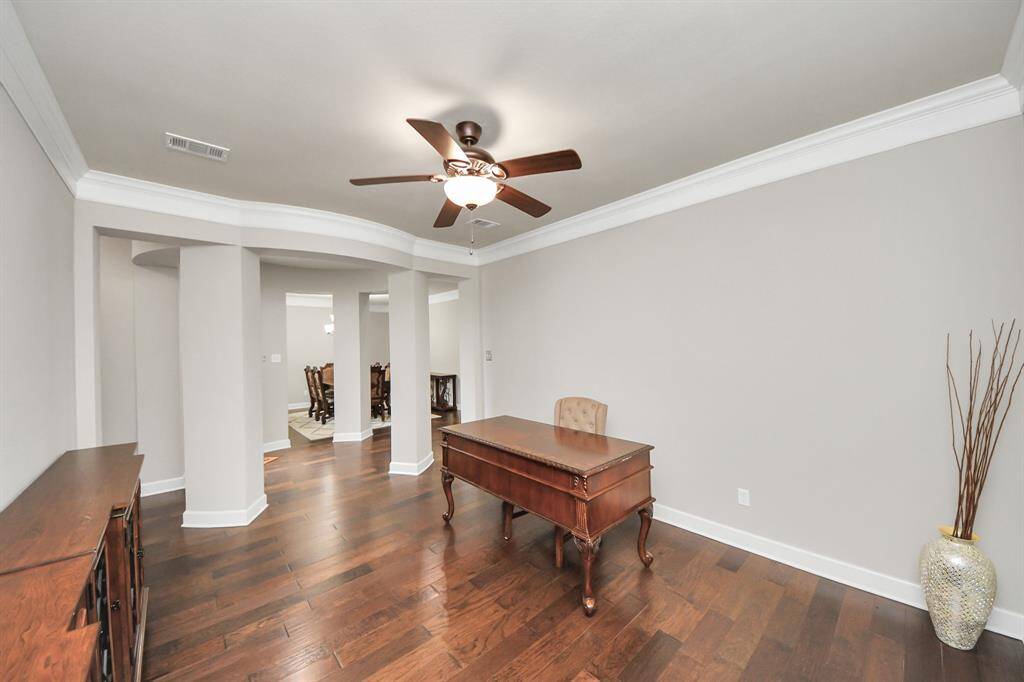 Spacious home office with hardwood floors, neutral walls, and a ceiling fan with lights open archway leading to the formal dining room.