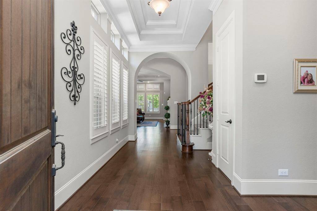 Step into a dramatic entry featuring high coffered ceilings trimmed with elegant crown molding. The gorgeous wood floors, custom baseboards, and tall interior doors throughout add a touch of luxury. A stunning entrance that’s sure to impress your family and guests as they enter your home!