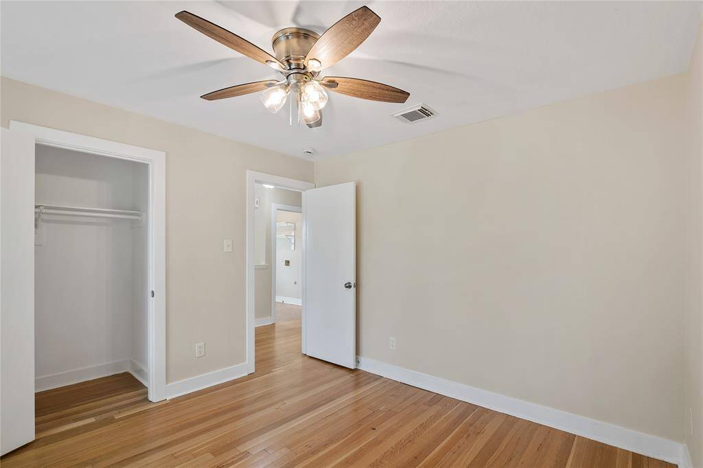 This is a bright, cozy room featuring hardwood floors, a ceiling fan with lights, and a small closet. The neutral wall color enhances the natural light, creating a welcoming atmosphere.