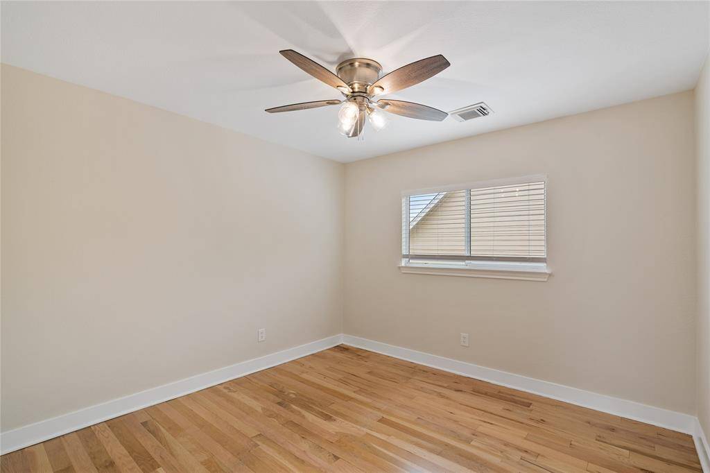 This room features hardwood flooring, neutral walls, and a ceiling fan with lights. A window with blinds provides natural light.