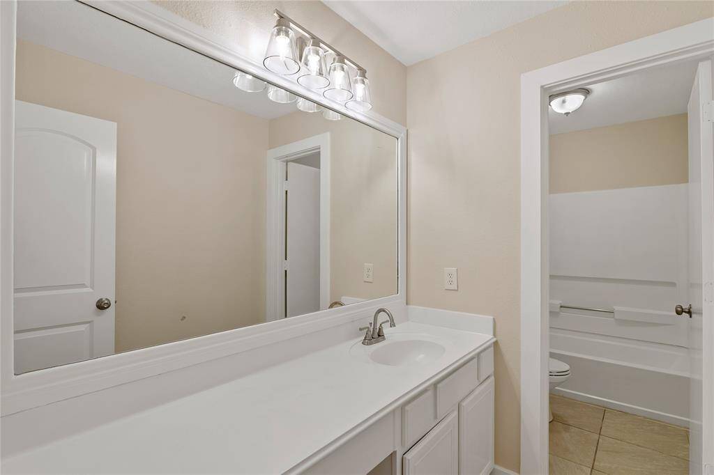This is a bright, modern bathroom featuring a large mirror, stylish lighting, and a white vanity with ample storage. It leads to a separate shower area, offering a clean and functional design.