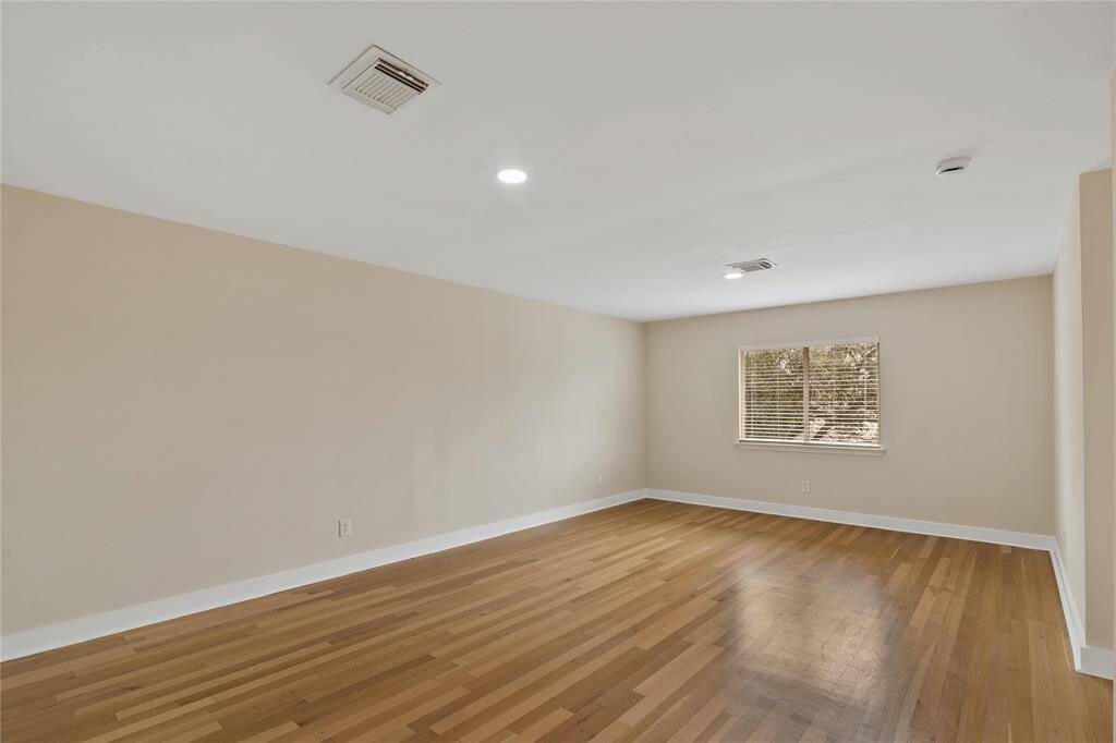 Spacious room with hardwood flooring, neutral walls, and ample natural light from a single window. Ceiling includes recessed lighting and air vents.