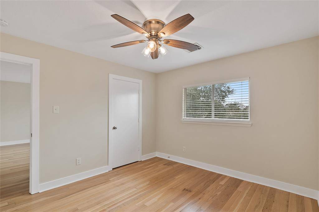 This photo shows a bright, empty room with light wood flooring, neutral walls, a ceiling fan with lights, and a window with blinds offering natural light. Ideal for a bedroom or home office.
