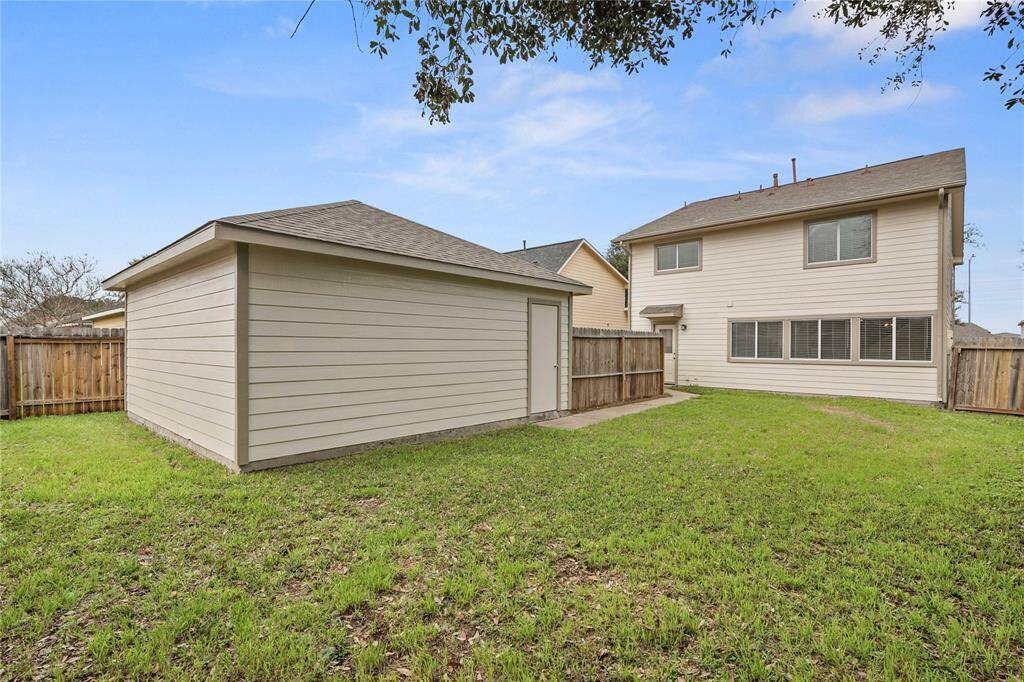 This photo shows a spacious backyard with green lawn, a detached garage, and a two-story house. The area is fenced, offering privacy and a good space for outdoor activities.