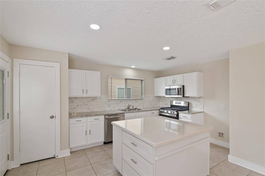 Modern kitchen with sleek white cabinetry, a central island, and stainless steel appliances. The space features a neutral color palette with tiled flooring and a marble-look backsplash, offering a bright and inviting atmosphere.
