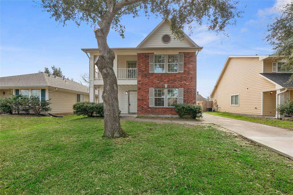 This two-story home features a charming brick facade with large windows, a welcoming porch, and a balcony on the upper floor. It is set on a spacious lot with a well-maintained lawn and driveway, providing ample outdoor space.