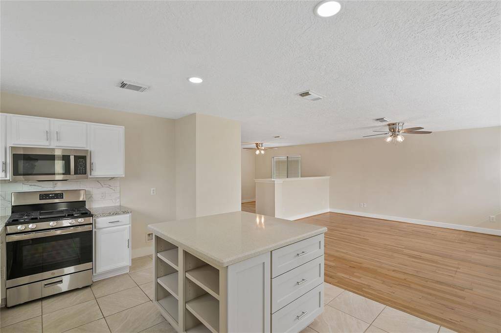 This photo showcases a modern, open-concept kitchen and living area. The kitchen features a sleek island, stainless steel appliances, and white cabinetry, leading into a spacious living room with hardwood floors and ceiling fans.
