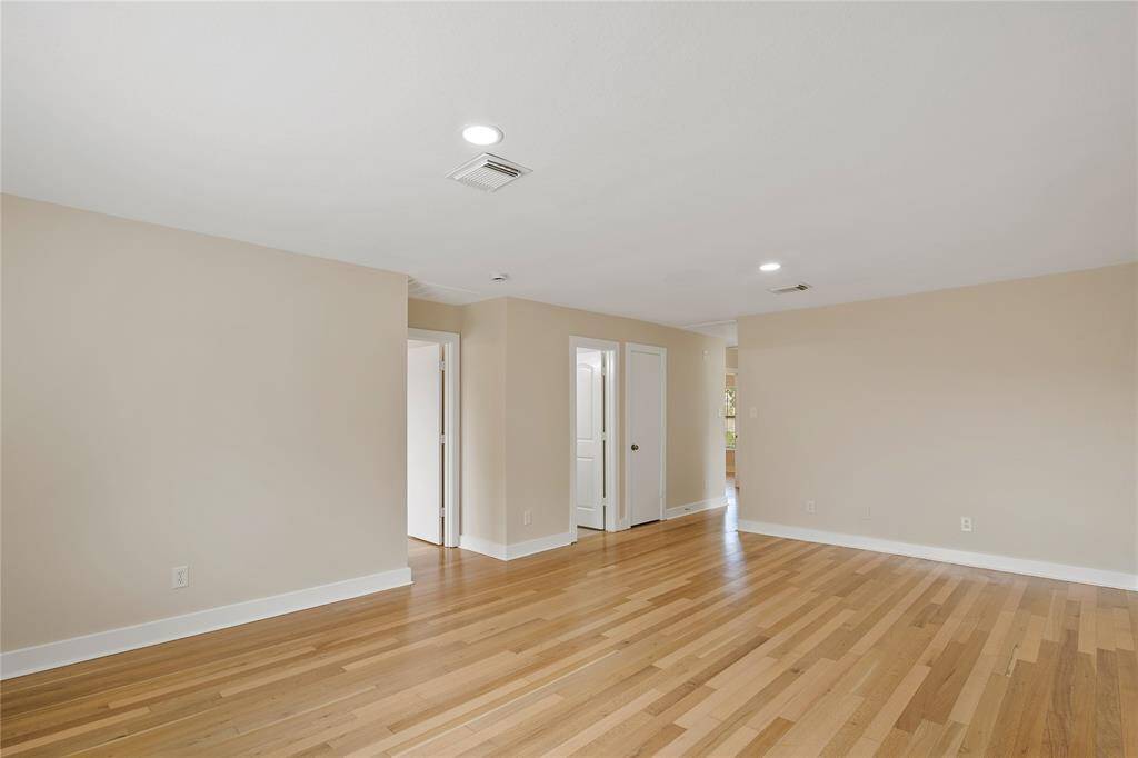 Spacious room with light wood flooring and neutral-colored walls, featuring recessed lighting. It includes a doorway leading to other parts of the home, offering a versatile layout.