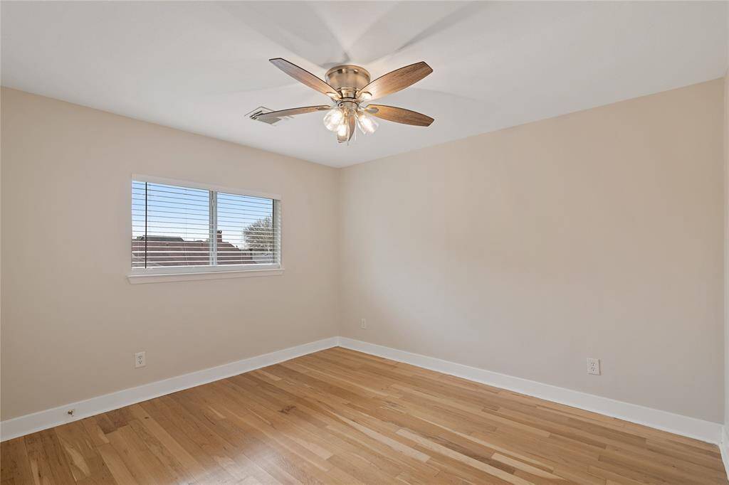 Bright, empty room with hardwood floors, a ceiling fan, and a window with blinds. Neutral wall color provides a blank canvas for personal touches.