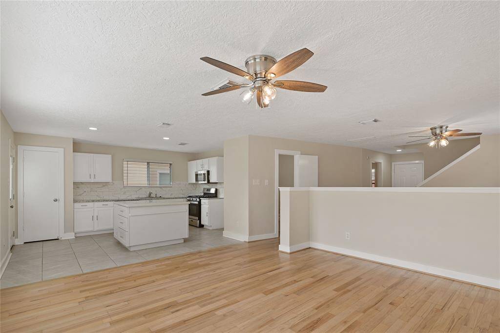 Bright and spacious open-concept living area with hardwood floors, a modern kitchen featuring white cabinetry, and an island. Ceiling fans provide comfort, and neutral tones create a welcoming atmosphere.