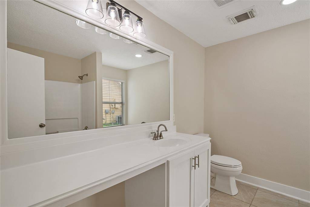 This bathroom features a modern vanity with a large mirror and stylish lighting. It includes a bathtub-shower combination, a toilet, and a window for natural light. The neutral color scheme enhances the spacious, clean look.