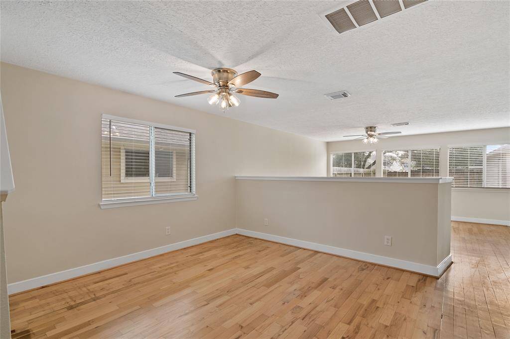 This bright and airy living space features light hardwood flooring, neutral walls, and large windows for ample natural light. Two ceiling fans enhance comfort, and a half-wall offers a subtle room division, ideal for versatile living arrangements.