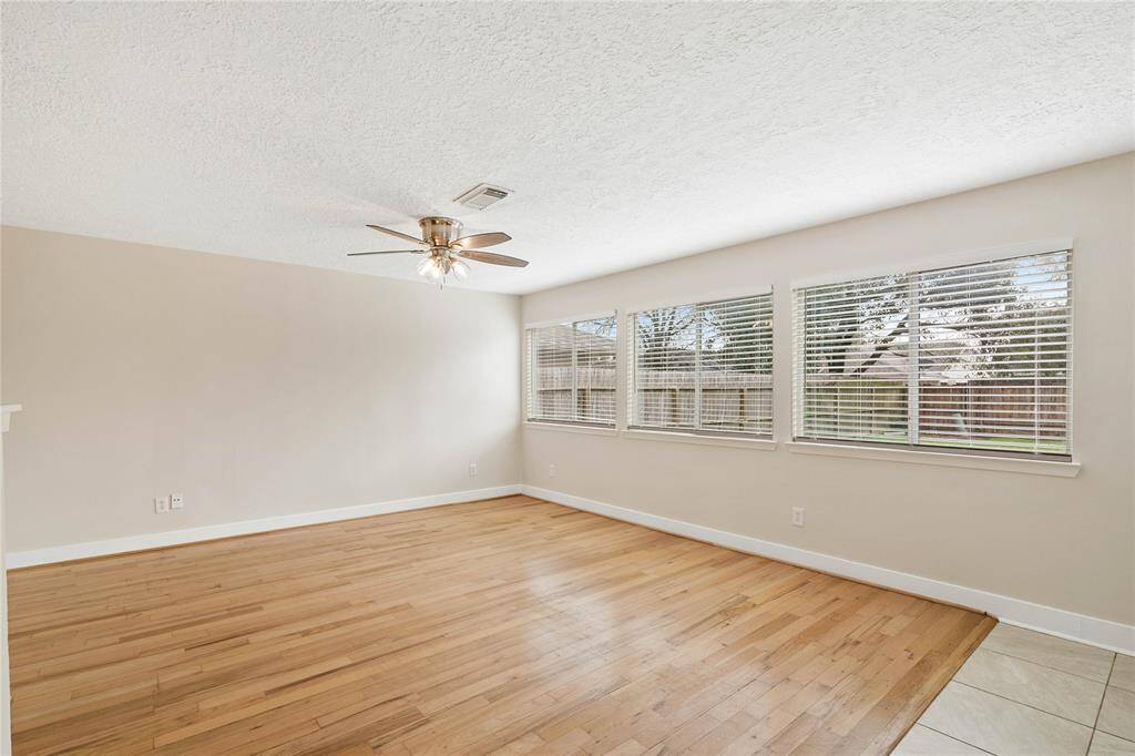 Bright and spacious room with large windows, hardwood floors, and a ceiling fan, offering a cozy and inviting atmosphere.