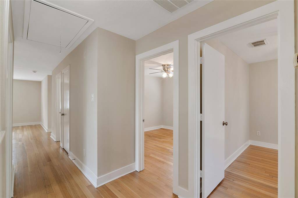 This photo shows a bright and clean hallway with hardwood floors and neutral walls. It leads to multiple rooms, one of which has a ceiling fan. The space feels open and inviting.