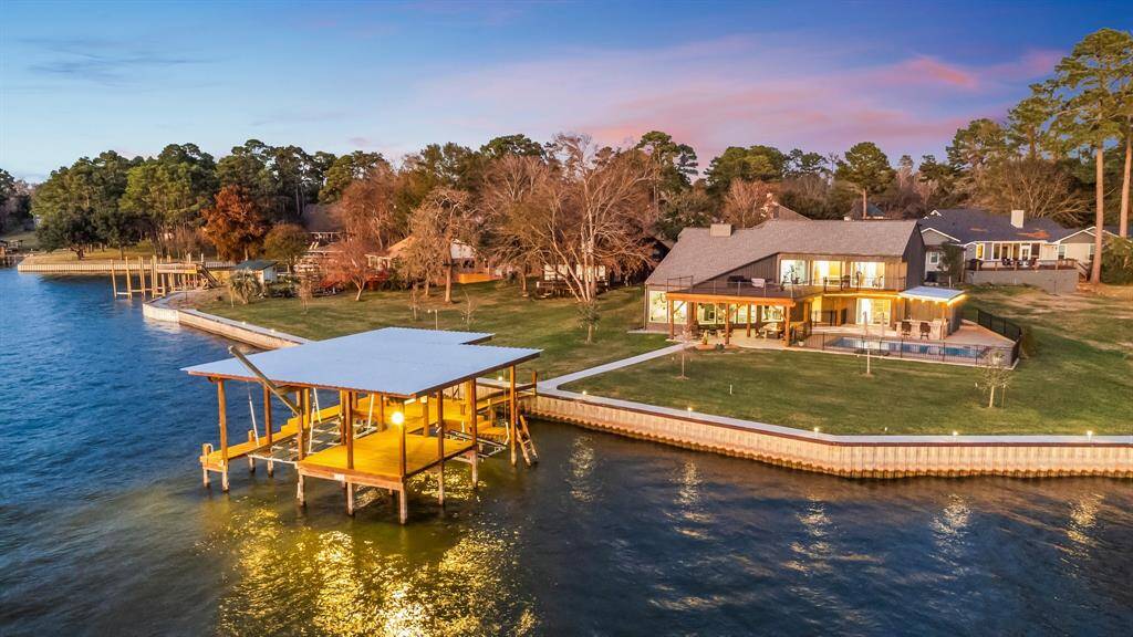 This photo showcases a stunning waterfront property with a spacious modern home and large windows, offering panoramic views. It features a well-maintained lawn, a private boat house, garage apartment, and plenty of outdoor space, perfect for enjoying serene lakeside living.