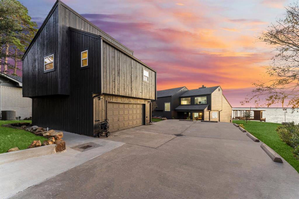 Modern two-story home with a sleek, dark wood exterior and spacious driveway. The property offers stunning sunset views.