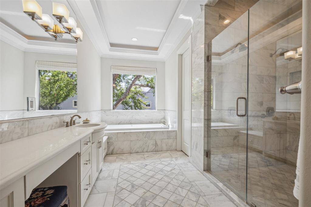 The primary bath is a spa-like retreat, featuring dual vanity areas and a shared glass-encased shower. One side boasts a generous soaking tub, perfect for unwinding after a long day.