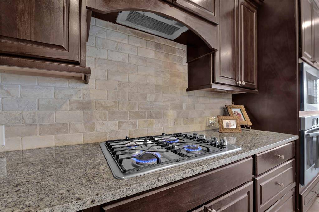 Encompassing the gas cooktop, are sleek granite countertops that provide a beautiful workspace. Their smooth surface is perfect for food preparation, while the elegant stone backsplash adds a touch of sophistication. The rich wood cabinetry introduces warmth & character.