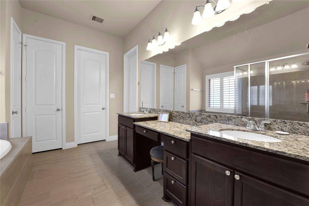 The luxurious ensuite bathroom of the primary retreat is a true oasis, featuring dual sinks set within sleek granite countertops and complemented by rich wood cabinetry.  A spacious sit-down vanity provides a convenient spot for your morning routines, making it easy to prepare for the day ahead.