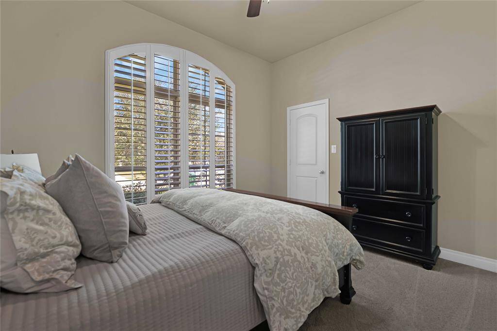 This spacious secondary bedroom offers ample room ensuring comfort. A large window with plantation shutters allows natural light to flow in while maintaining privacy. The plush carpet underfoot adds warmth, & the high ceiling with a ceiling fan enhances the room’s airy feel. A generous walk-in closet provides plenty of storage.