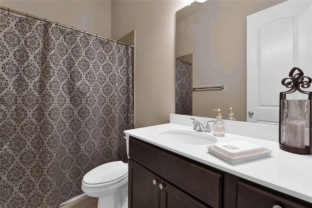 The secondary bathroom designed for sharing features a sleek countertop paired with rich wood cabinetry below. Above, a large frameless mirror reflects light beautifully, complemented by stylish vanity lighting. The spacious tub and shower combo offers versatile use, making it ideal for quick showers or relaxing baths.