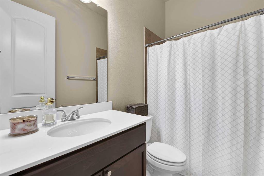 The secondary bathroom features a sleek countertop paired with rich wood cabinetry below. Above, a large frameless mirror reflects light beautifully, complemented by stylish vanity lighting.The spacious tub and shower combo offers versatile use, making it ideal for quick showers or relaxing baths.
