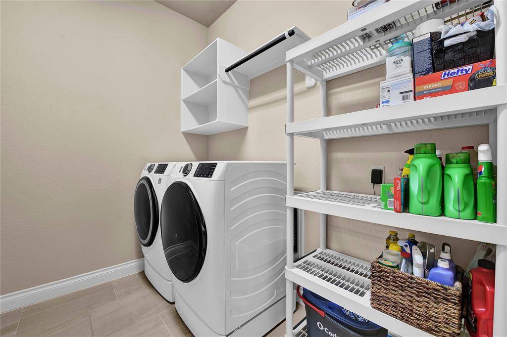 A spacious laundry room provides ample room for a full-size washer & dryer, along with additional space for a deep freezer or 2nd fridge. Thoughtfully designed, the room includes storage above the laundry machines & a convenient hanging rod, offering practical solutions for completing laundry tasks while keeping organized.