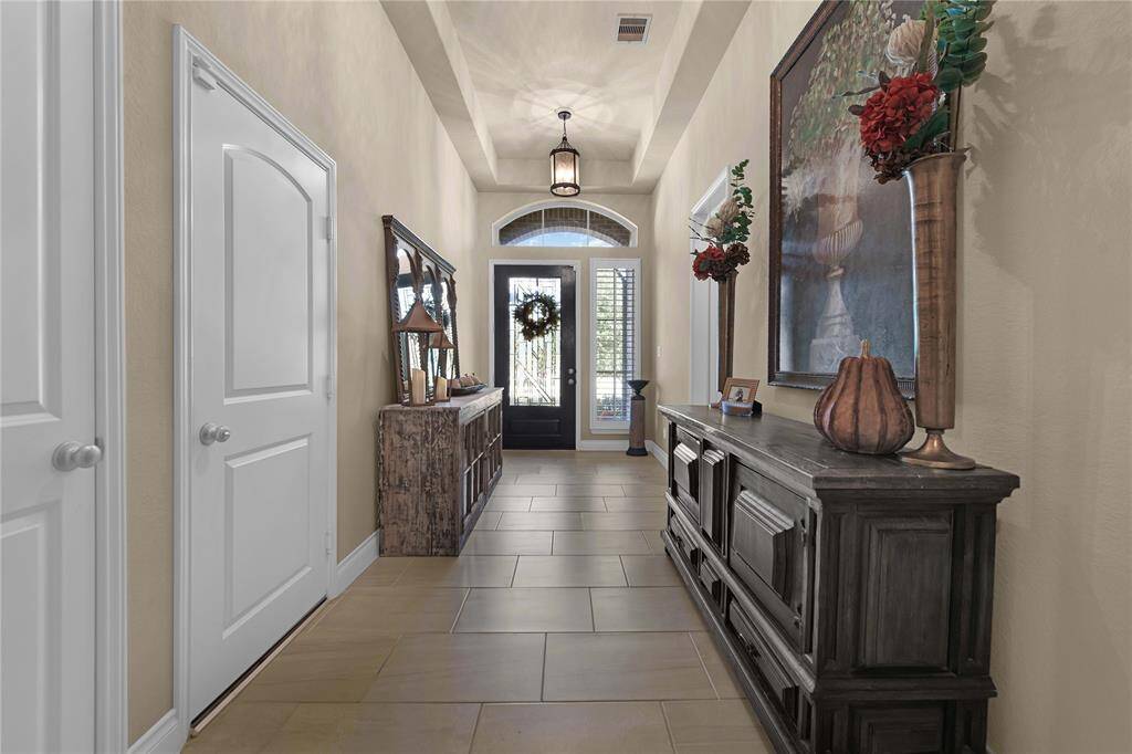 Step through the impressive 8-foot mahogany wood door, featuring a stunning leaded glass window, flanked by a sidelight and a sunburst window. The high tray ceiling creates an airy atmosphere, while the sleek elongated tile floors add a modern touch, enhancing the welcoming feel of the entryway.